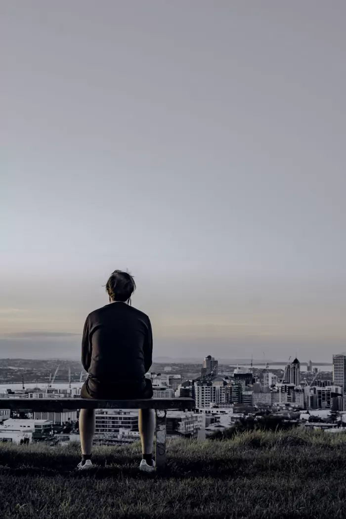 Person sitzt auf einer Bank und blickt über eine Stadt im Dämmerlicht